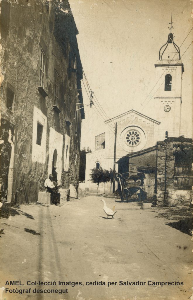 El masover de Can Ramoneda, Bru Campreciós, assegut al pedrís. Al fons, l’església parroquial de Santa Magdalena. 1914.